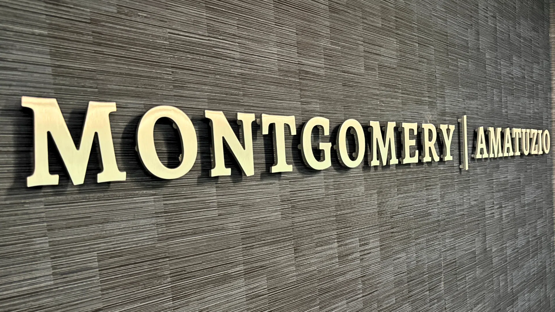 Brushed metal dimensional lobby sign with raised letters mounted on textured wall for professional office branding