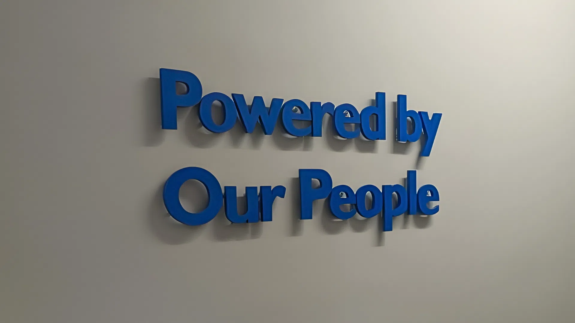 Dimensional blue wall lettering in a Denver corporate office reading ‘Powered by Our People,’ showcasing modern workplace branding