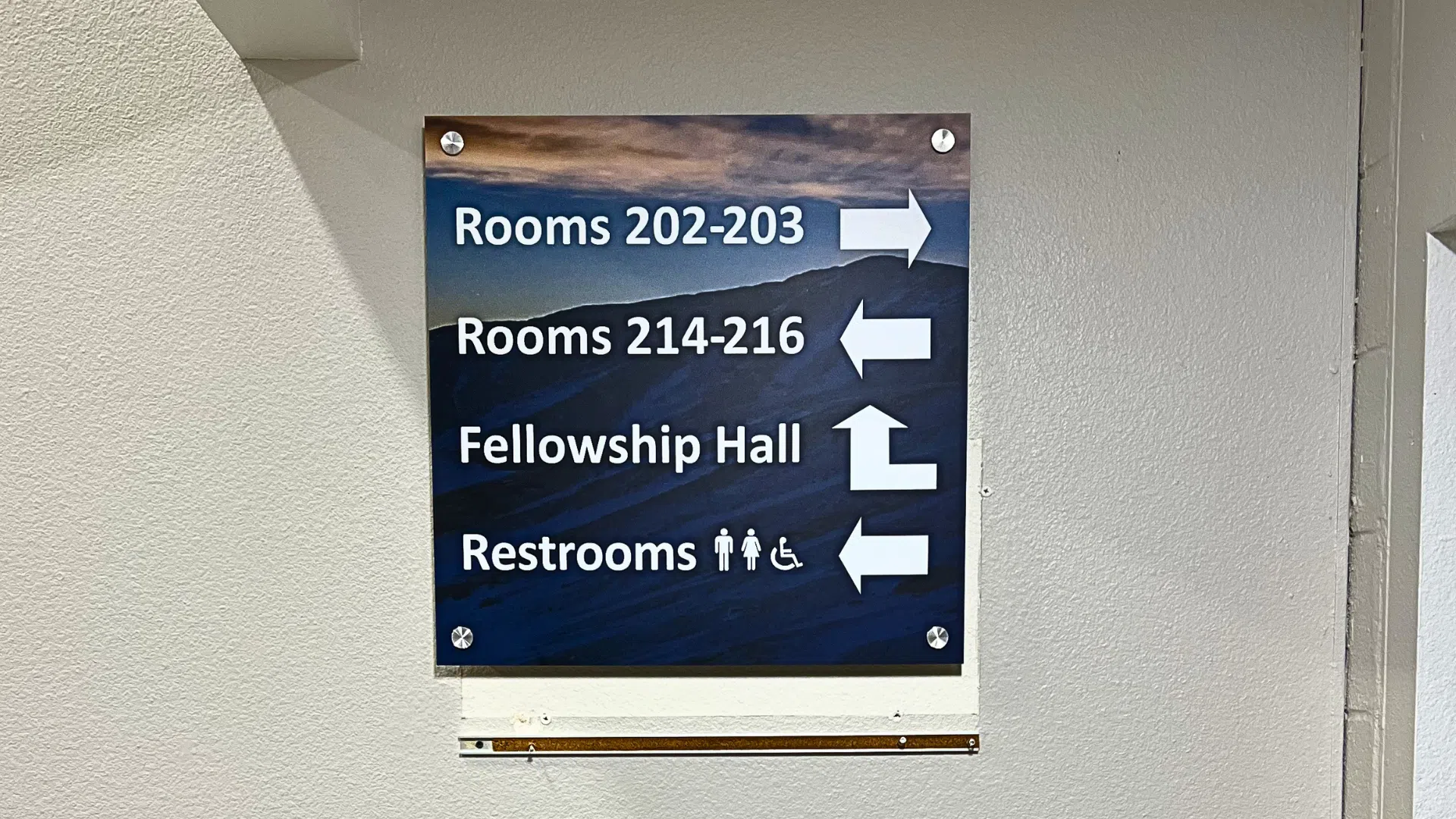 Interior wayfinding sign in a Denver multifamily property showing directions to rooms, fellowship hall, and restrooms with accessibility icons