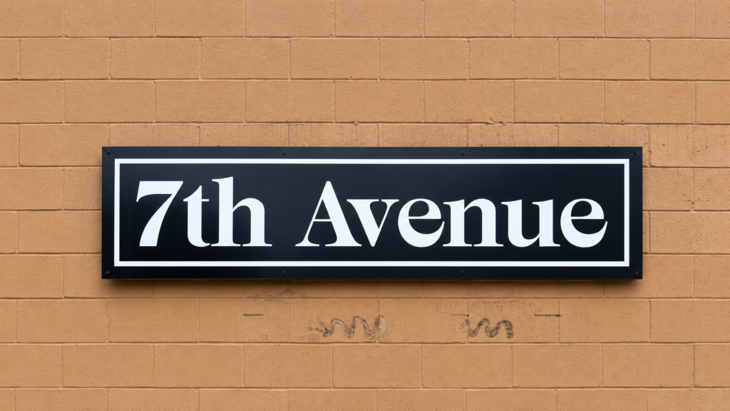 Rectangular 7th Avenue exterior business sign with white lettering and border mounted on a tan commercial building.