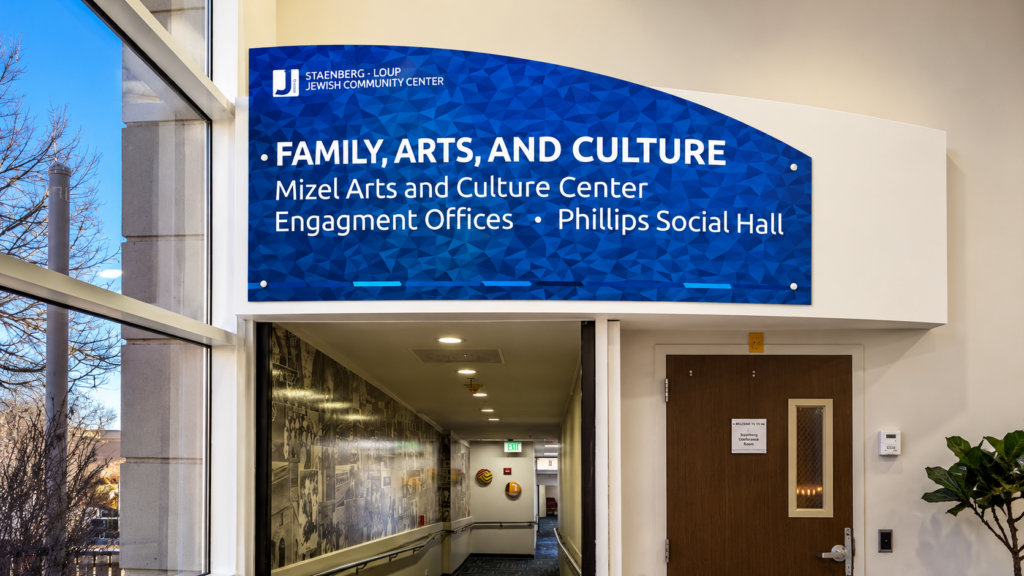 Blue interior wayfinding sign identifying the Mizel Arts and Culture Center, Engagement Offices, and Phillips Social Hall.