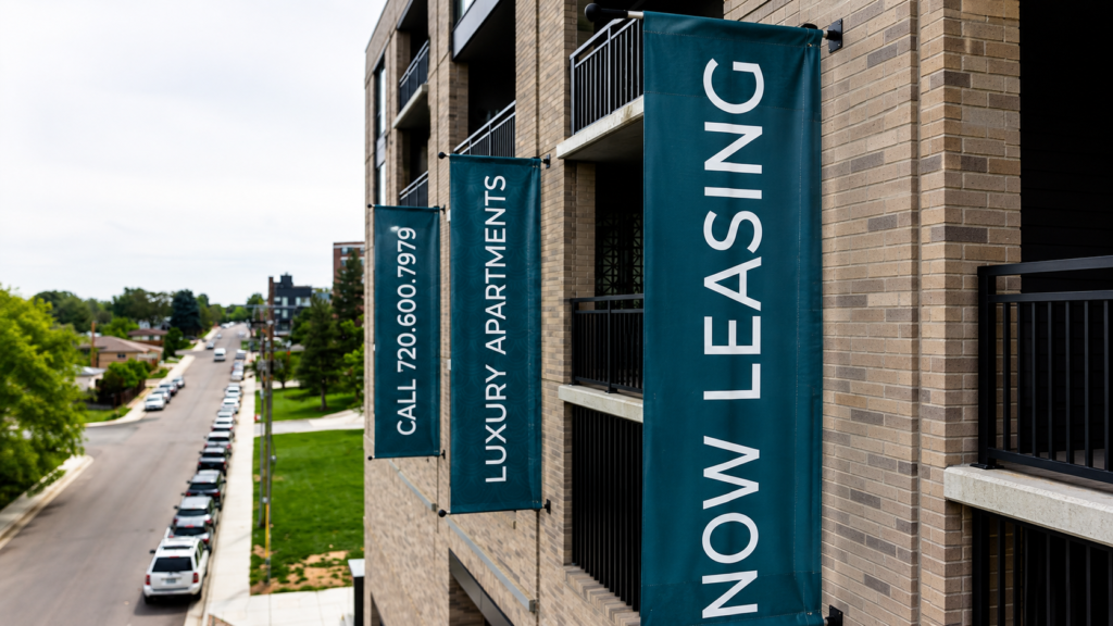 Three teal projecting banners advertising Now Leasing, Luxury Apartments, and a leasing phone number on a multifamily building.
