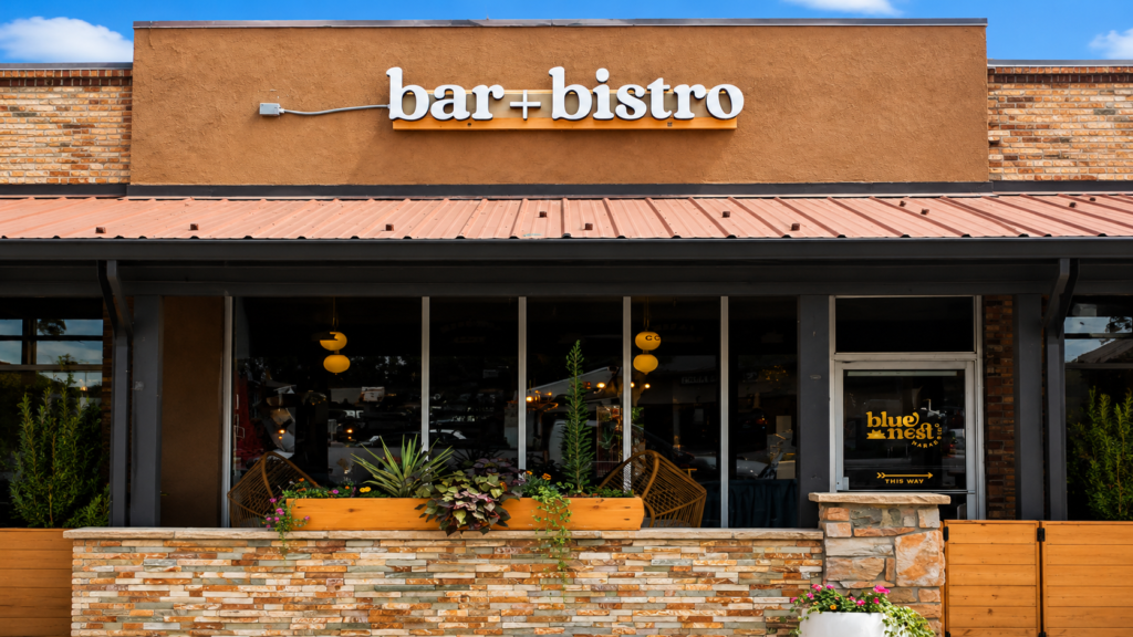 White dimensional Bar + Bistro letters mounted above the entrance of a restaurant storefront with windows and outdoor planters.