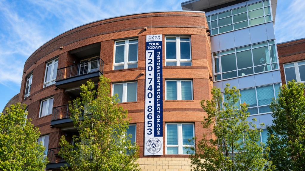 Large vertical Tour Today leasing sign displayed on the exterior of a modern multifamily apartment building in Colorado.
