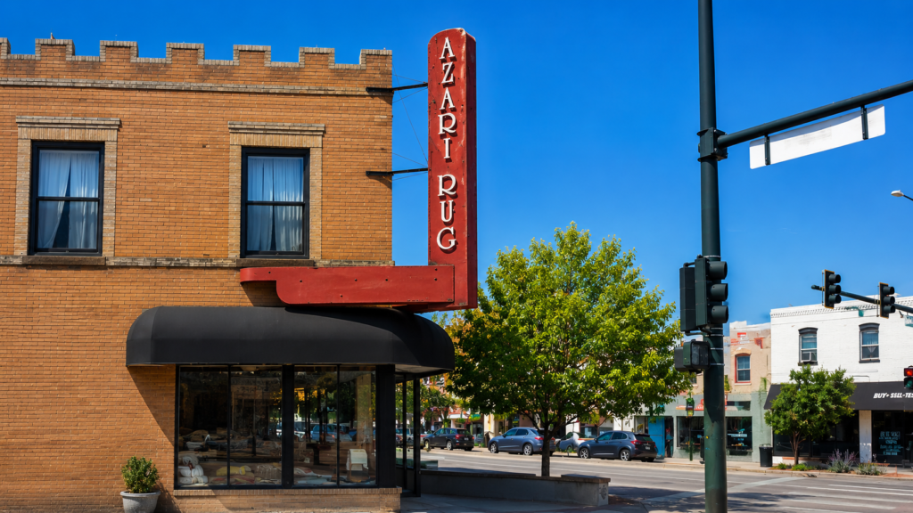 Vintage vertical Azari Rug storefront sign projecting from a brick retail building for visibility from the street.