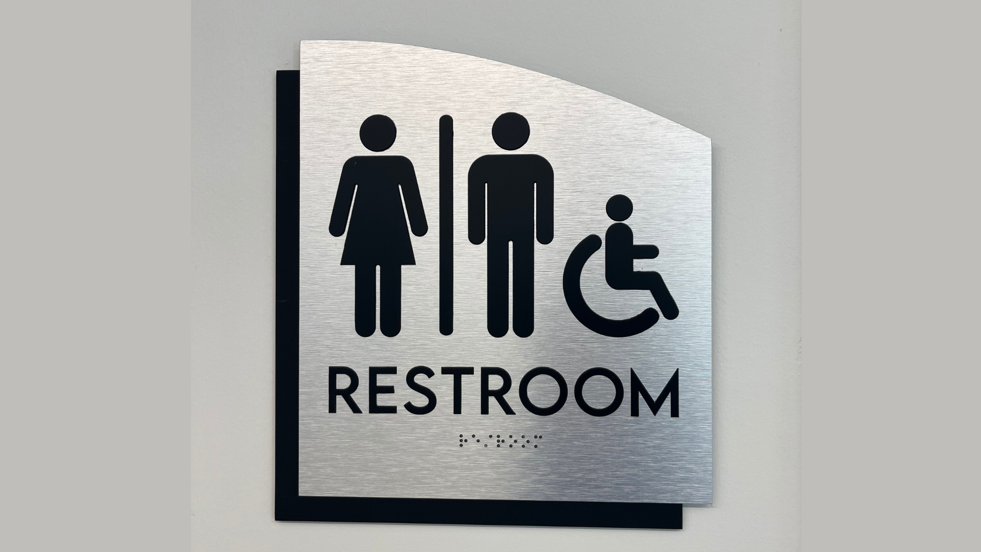 ADA-compliant restroom sign with tactile lettering, Braille, and accessibility symbols installed inside a commercial building in Denver, Colorado.