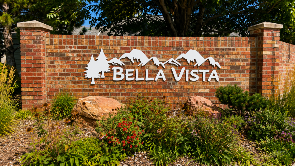 Bella Vista entrance monument sign with white mountain and tree graphics mounted on a landscaped brick wall.
