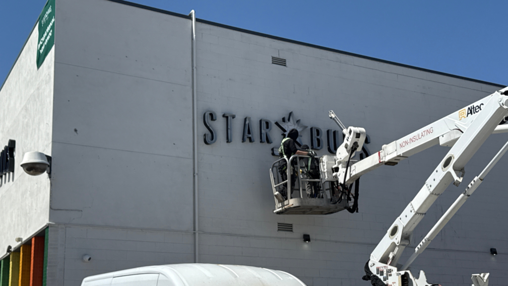 Sign technician using an aerial lift to install dimensional building letters on a commercial exterior wall