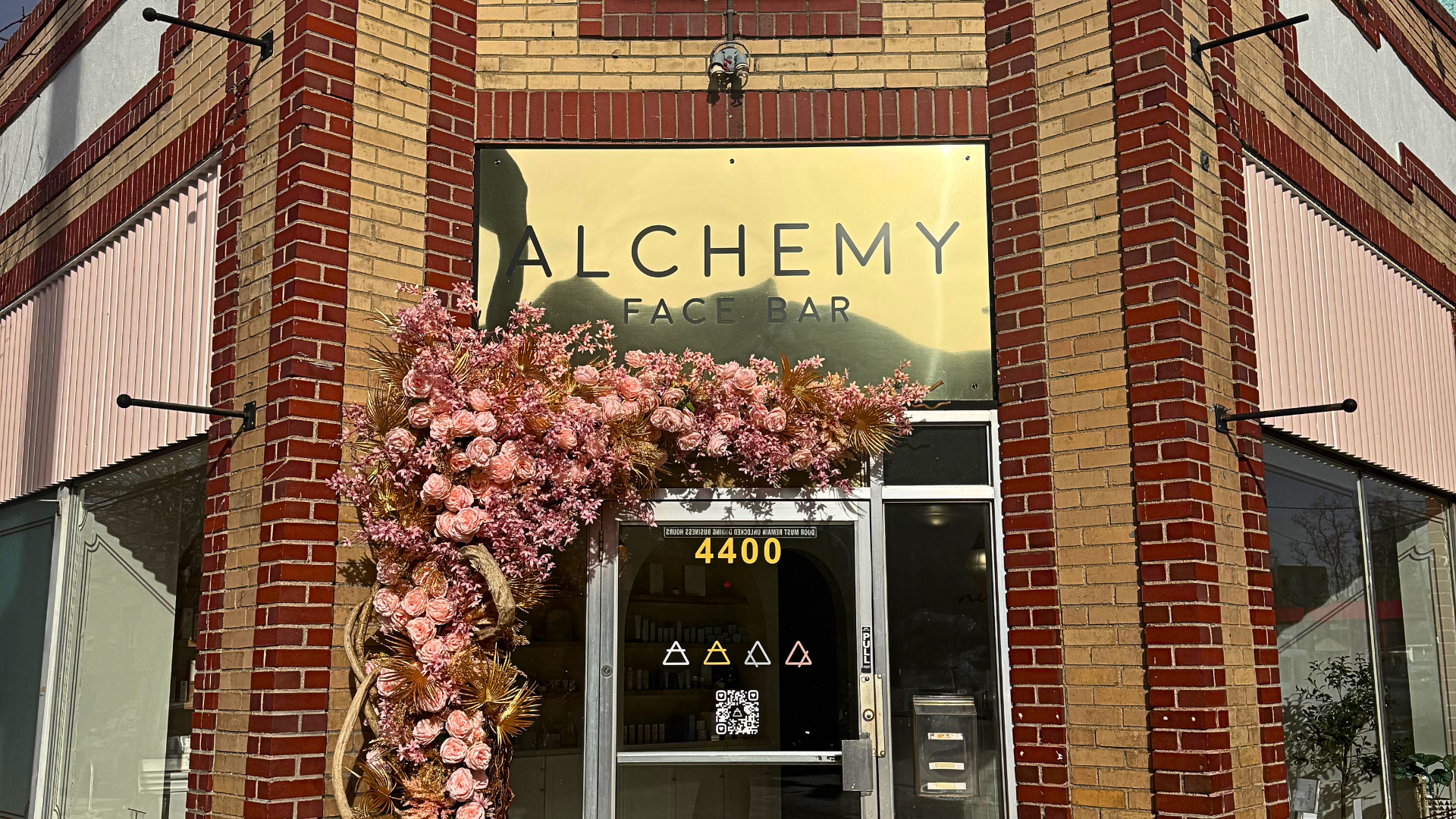 Custom commercial storefront sign for Alchemy Face Bar in Denver, Colorado featuring a polished gold business sign and decorative floral entrance display.